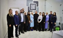 Група людей стоїть перед логотипом установи, позуючи для фото.