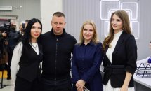 Група людей стоїть перед логотипом установи, позуючи для фото.