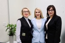 Три жінки усміхаються на фоні логотипа організації.