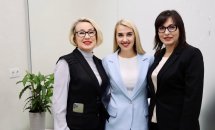 Три жінки усміхаються на фоні логотипа організації.