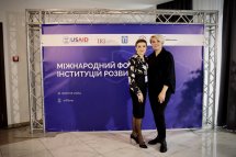 Двоє учасників заходу позують перед стендом із логотипами організаторів.