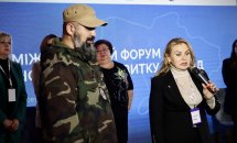 Жінка з мікрофоном та чоловік у військовій формі беруть участь у дискусії.