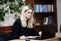 Світловолоса жінка у чорному светрі сидить, працюючи за ноутбуком.