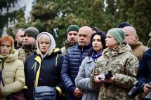 Група людей, серед яких військові та цивільні, стоять разом, виглядають серйозними.