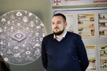 Чоловік стоїть біля інформаційного стенду, на фоні якого зображені схеми та діаграми, що стосуються цифрових технологій.