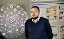 Чоловік стоїть біля інформаційного стенду, на фоні якого зображені схеми та діаграми.