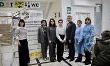 Двоє медпрацівників та п'ятеро людей стоять у приміщенні з табличками та вказівниками.