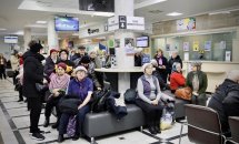 Люди сидять у черзі на стільцях у великому залі з яскравим освітленням.