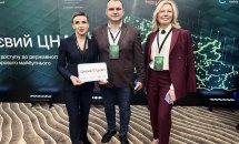 Троє людей позують для фото, одна людина тримає сертифікат.