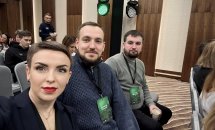 Селфі трьох людей у конференц-залі, двоє чоловіків і жінка на передньому плані.
