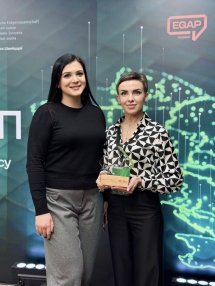 Дві жінки позують перед зеленою фоновою стіною з цифровими елементами.