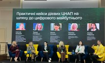 Панельна дискусія на конференції, спікери сидять у жовтих кріслах на сцені.