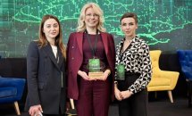 Дві жінки стоять біля стенду конференції, одна тримає нагороду.
