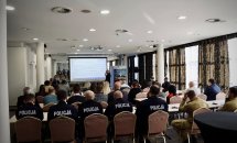 Велика кількість людей сидить у конференц-залі, на передньому плані видніється проєкційний екран.