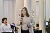 Жінка з мікрофоном: Учасниця конференції виступає перед аудиторією, поруч сидить інша жінка.