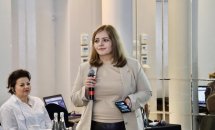 Жінка з мікрофоном: Учасниця конференції виступає перед аудиторією, поруч сидить інша жінка.