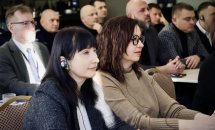 Учасниці конференції уважно слухають доповідь, на задньому плані сидять інші учасники.