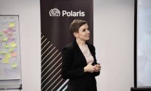 Жінка перебуває в офісі. Вона одягнена у діловому стилі та має коротку зачіску.