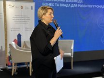 Жінка тримає у руках мікрофон та проголошує доповідь.