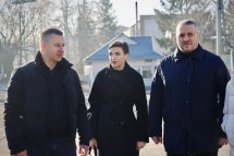 Двоє чоловіків і жінка стоять на вулиці, обговорюючи щось. На задньому плані видно міські будівлі