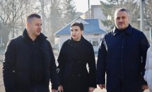 Двоє чоловіків і жінка стоять на вулиці, обговорюючи щось. На задньому плані видно міські будівлі