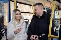 Жінка посміхається та тримає картку. Поруч стоїть чоловік, на задньому плані видно салон транспорту