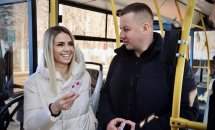 Жінка посміхається та тримає картку. Поруч стоїть чоловік, на задньому плані видно салон транспорту