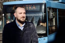 Чоловік стоїть на вулиці. На задньому плані видно тролейбус