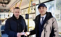 Двоє чоловіків у тролейбусі дивляться в камеру, тримаючи в руках картку.