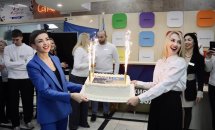 Дві жінки посміхаються та тримають у руках торт. На задньому фоні люди посміхаються.