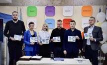 Чоловіки та жінки стоять у приміщені  ЦНАПу в місті Рівному та тримають у руках марки.