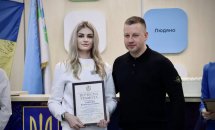 Чоловік та жінка стоять у приміщені  ЦНАПу в місті Рівному. Жінка тримає у руках почесну грамоту.