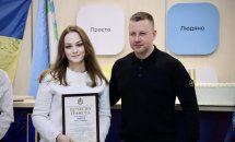 Чоловік та жінка стоять. Жінка тримає у руках почесну грамоту.