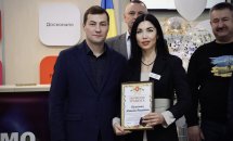 Чоловік та жінка стоять у приміщені  ЦНАПу в місті Рівному. Жінка тримає у руках почесну грамоту.