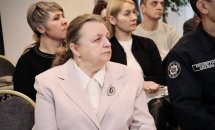 Жінка поважного віку сидить та слухає на діалоговій зустрічі.