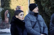 Жінка з коротким волоссям у верхньому одязі чорного кольору та чоловік в головному уборі та синій куртці стоять на дворі.