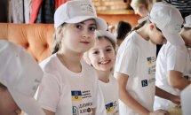 Діти у білих футболках посміхаються.