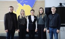 Група людей з двох чоловіків та трьох жінок стоять у приміщенні на фоні карти Рівненської області.