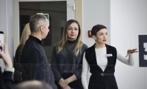 Працівниця у чорному жилеті з бейджем показує для чоловіка та жінки приміщення ЦНАПу у місті Рівне.