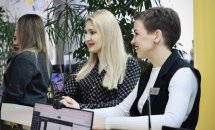 Дві жінки стоять біля столу та усміхаються, спілкуючись із працівницею установи.