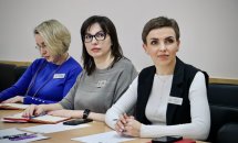 Три жінки з бейджами сидять за столом, дивлячись убік лектора.