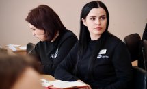 Дві жінки з темним волоссям та в чорних кофтах сидять за столом.