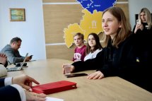 Дівчинка сидить за столом та тримає стакан з водою у руках.