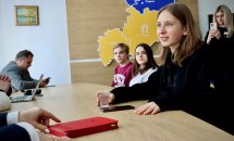 Дівчинка сидить за столом та тримає стакан з водою у руках.