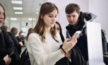 Дівчина тримає у руках телефон, біля неї стоїть хлопець та ще двоє дівчат.