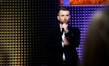 Чоловік у діловому костюмі тримає у руках мікрофон.