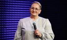 Жінка у вишиванці з короткою зачіскою та окулярах тримає мікрофон.