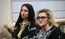 Дві жінки у чорних вишиванках сидять у приміщенні.