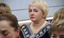 Жінка зі світлим коротким волоссям та у вишиванці сидить у залі.