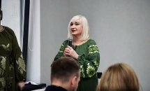 Жінка у вишитій сукні тримає мікрофон у руках.